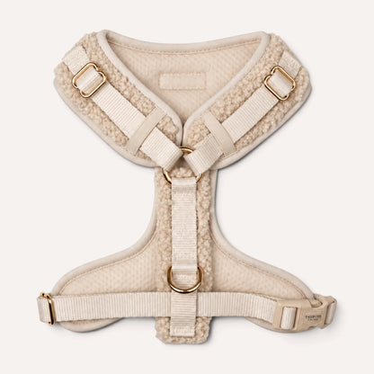 A cream-colored dog harness with a textured fleece-like fabric and gold-tone metal hardware, shown against a solid off-white background.