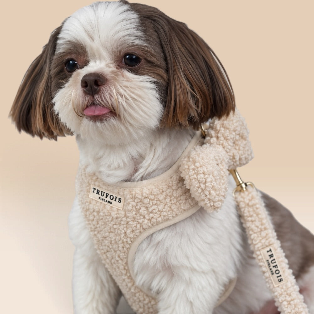 A small Shih Tzu dog wearing a cream-colored sherpa fleece dog harness and matching leash with a visible 'TRUFOIS' brand patch, set against a solid beige background.
