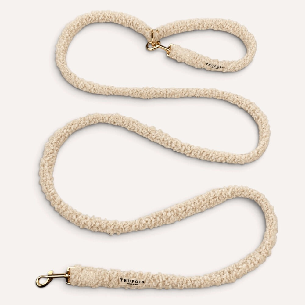 A beige sherpa fleece dog leash with gold-tone hardware, shown coiled on a light cream background. The brand name 'TRUFOIS' is printed on the leather end caps.