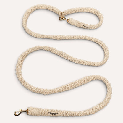 A beige sherpa fleece dog leash with gold-tone hardware, shown coiled on a light cream background. The brand name 'TRUFOIS' is printed on the leather end caps.