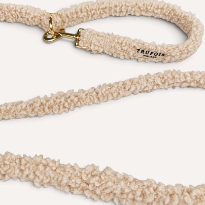 A close-up of a beige sherpa fleece dog leash with a gold-tone metal clasp and a small black 'TRUFOIS' brand tag, set against a clean off-white background.