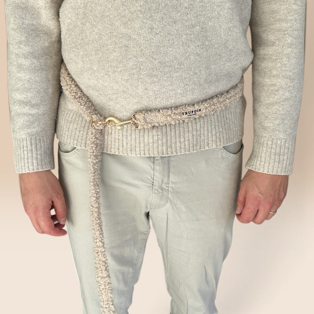 A close-up of a person wearing a light gray knit sweater and pale pants, with a beige textured belt wrapped around the waist and a gold-tone clasp. 