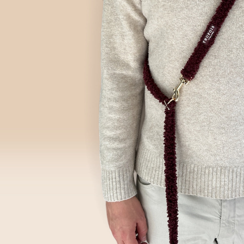 a dark burgundy fuzzy teddy dog leash across their chest with a gold-tone clasp. The strap has white text reading TRUFOIS.
